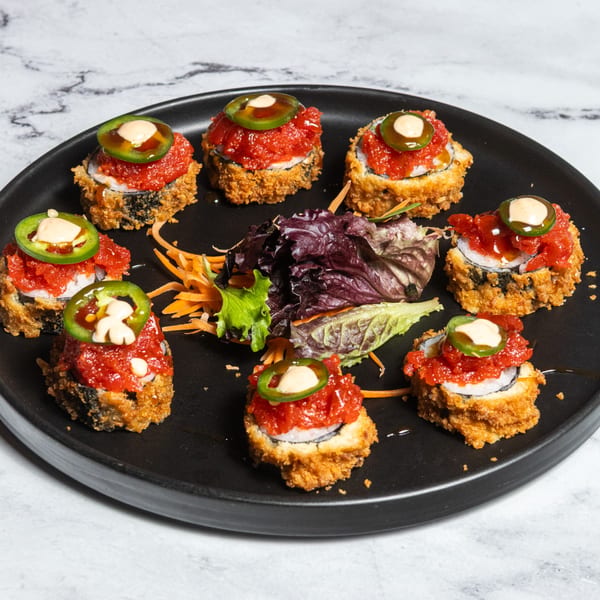 Eight deep-fried sushi rolls topped with red tuna, jalapeño slices, and creamy sauce on a black plate.