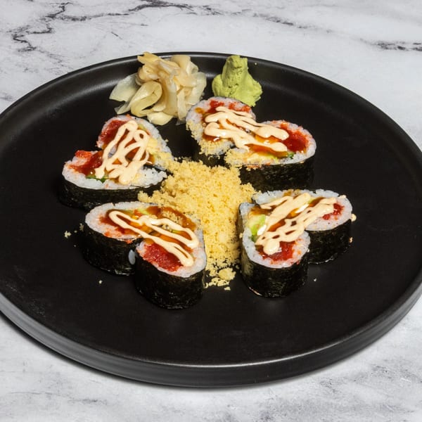 Heart-shaped sushi rolls with spicy tuna, sauce, and tempura flakes on a black plate.