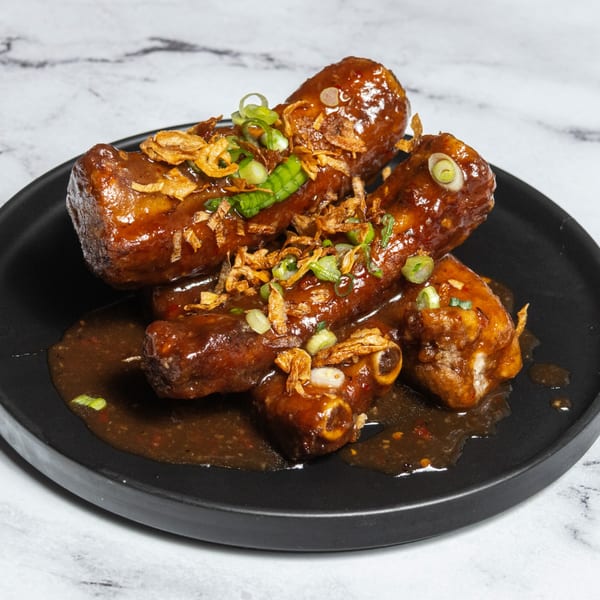 Ramen Lab Eatery's glazed pork ribs with crispy fried onions and chopped scallions on a black plate.
