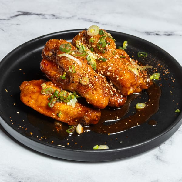Ramen Lab Eatery's crispy chicken wings, glazed with sauce, sesame seeds, and green onions on a black plate.