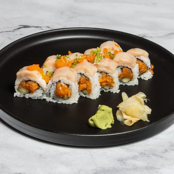 A black plate holds eight sushi rolls topped with fish, roe, and green onions, with wasabi and ginger.