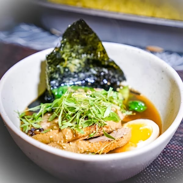 A bowl of Ramen Lab Eatery's ramen with sliced pork, a soft-boiled egg, greens, and nori.