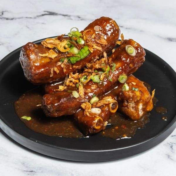 Braised pork ribs in a rich brown sauce, garnished with fried shallots and green onions on a black plate.