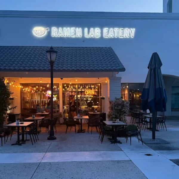 Exterior of Ramen Lab Eatery at dusk, with glowing sign, string lights, and outdoor seating.