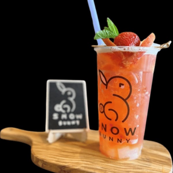 Strawberry drink with mint and fruit slices, next to a "Snow Bunny" sign on a wooden board.
