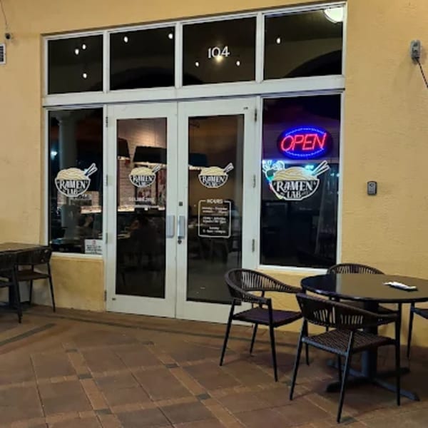 Exterior of Ramen Lab Eatery with an 'OPEN' neon sign and outdoor seating at dusk.