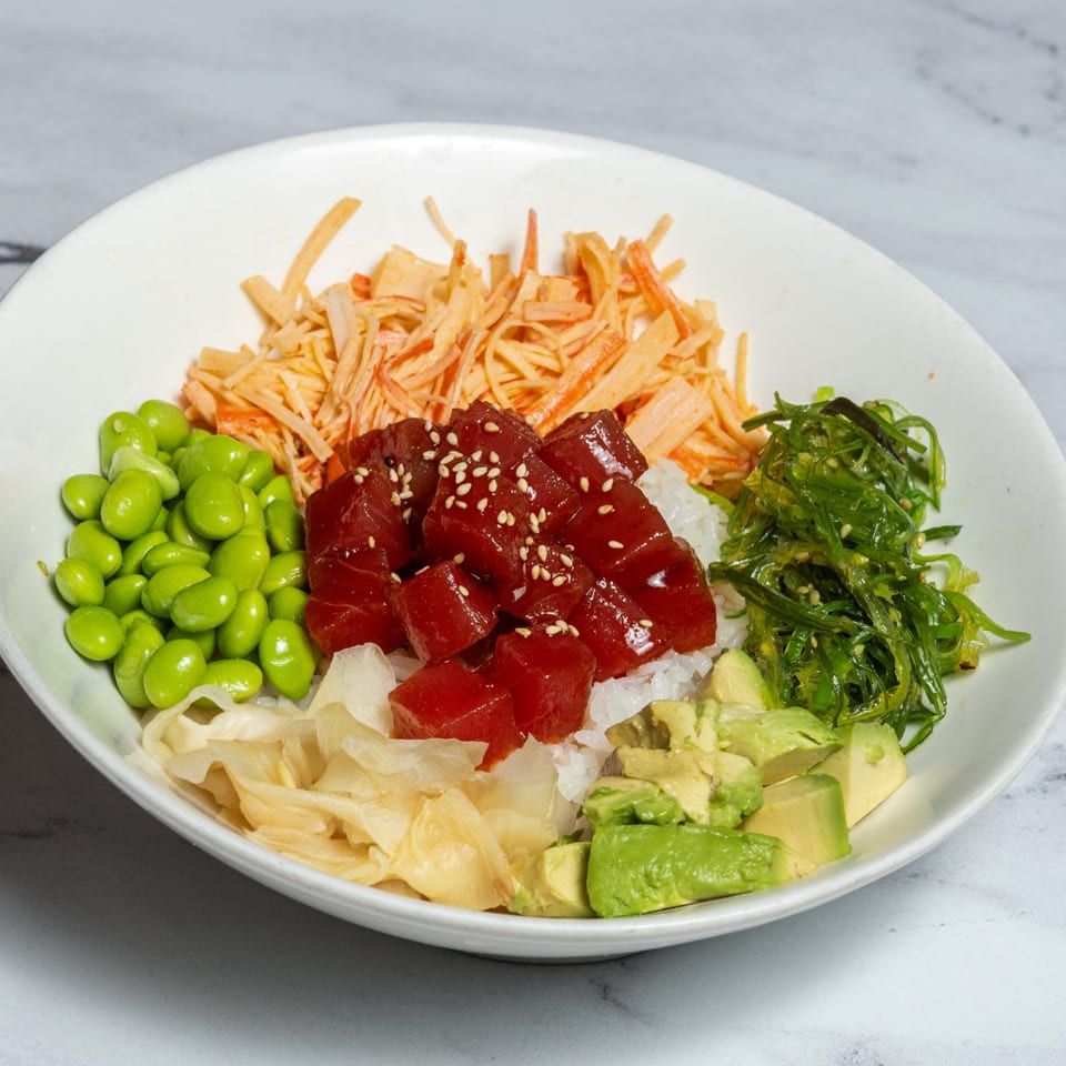 A colorful poke bowl with tuna, edamame, seaweed salad, avocado, and imitation crab.
