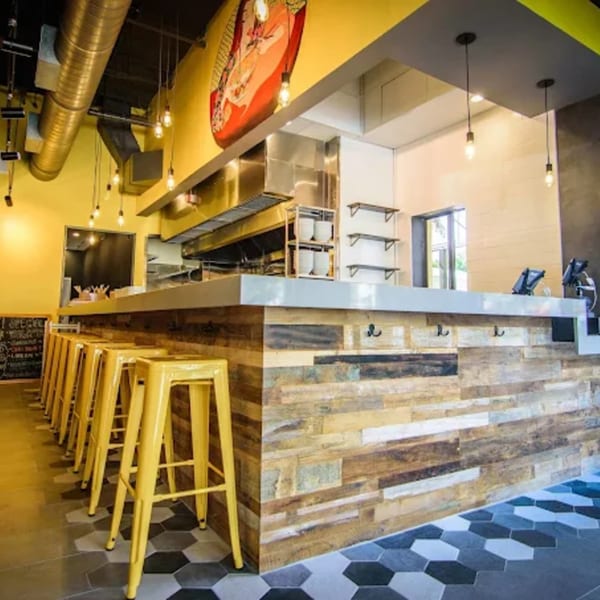 Ramen Lab Eatery's counter with yellow bar stools, a large ramen bowl mural, and industrial-style lighting.
