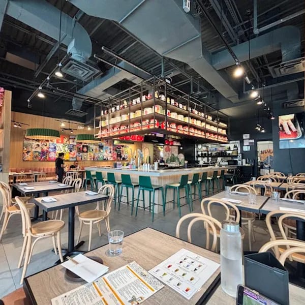 Interior of Ramen Lab Eatery with dining tables, bar seating, and shelves of Maneki-neko cats.