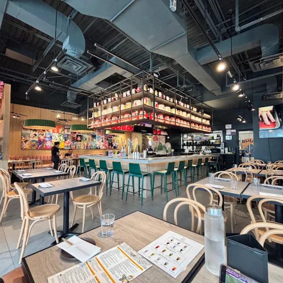 Interior of Ramen Lab Eatery with dining tables, bar seating, and shelves of Maneki-neko cats.